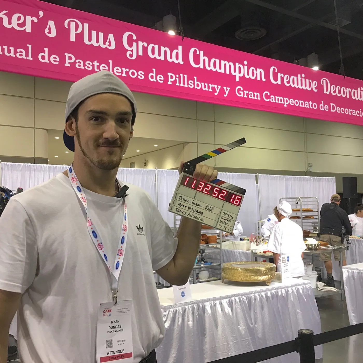 Ryan holding a clapperboard on the floor of a baking-championship event
