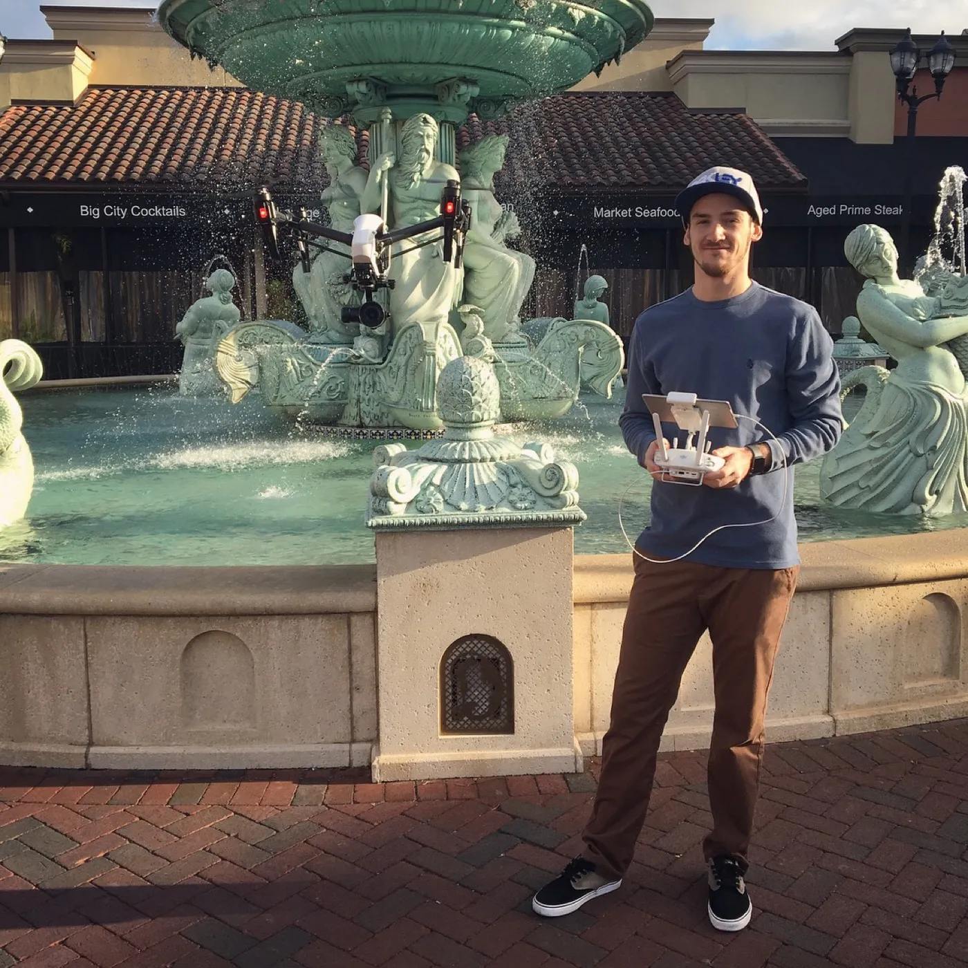 Ryan flying a drone over an ornamental fountain at an outdoor shopping plaza